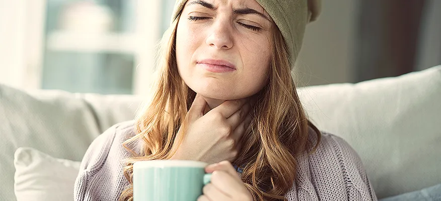 A woman with a distressed expression holding her throat and a mug, wondering if can coffee make you cough