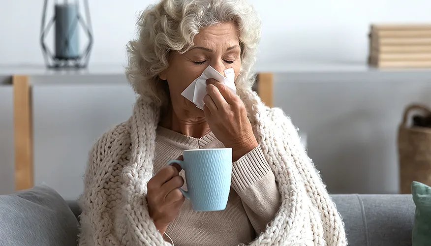 A person with a cough holding a cup of hot coffee, considering the downsides of whether can coffee help with colds.